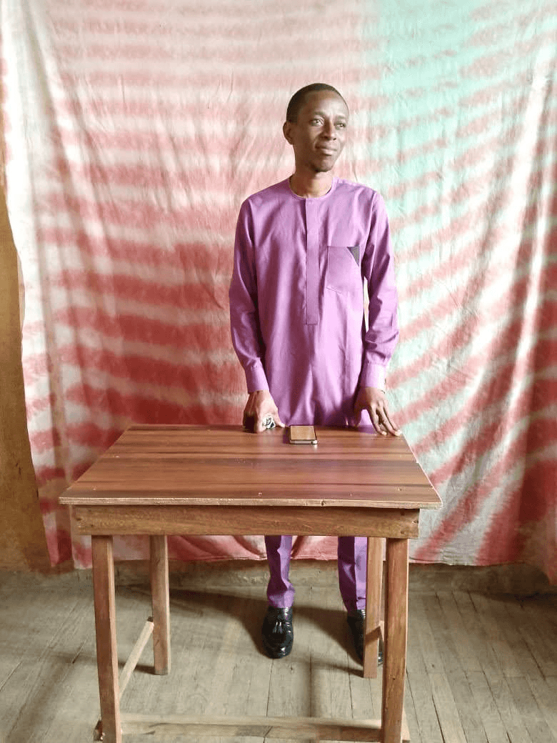 A man standing behind a wooden table in a classroom.