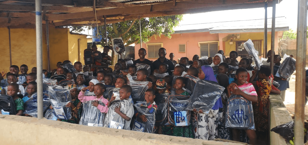 A large group of smiling children holding new school bags still in their wrapping.